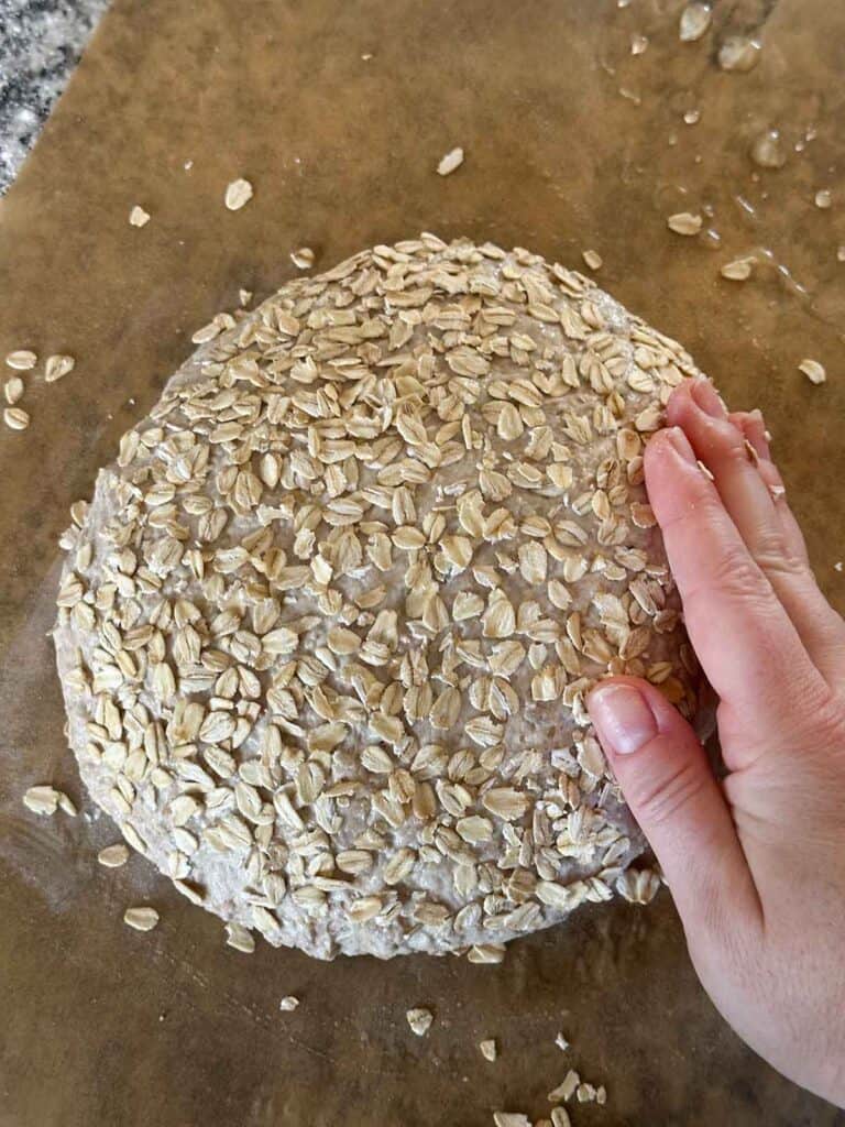 Pressing oats onto the surface of a round loaf of bread before baking.