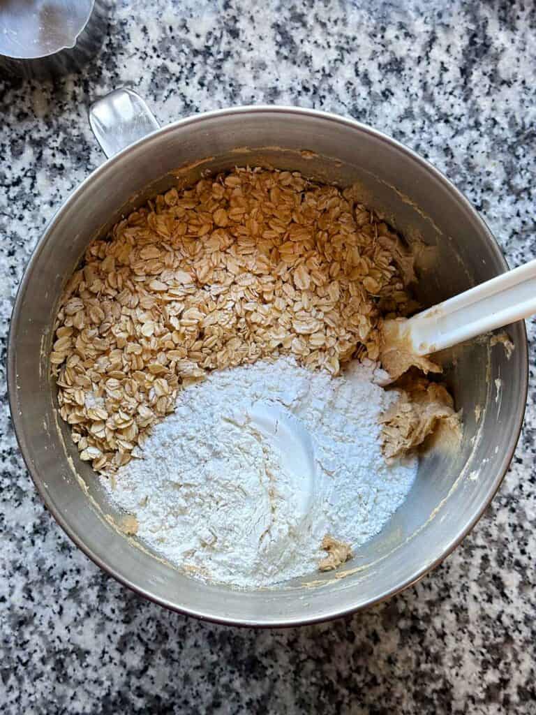 A mixing bowl showing oats and flour being added to cookie dough.