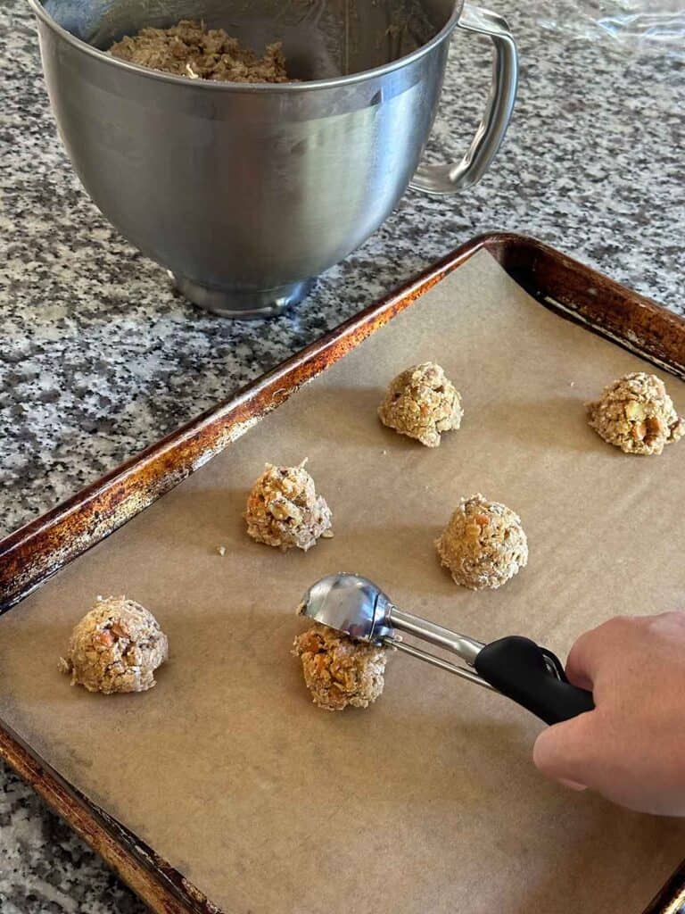A hand using a cookie scoop to scoop cookie batter onto a parchment covered baking sheet.