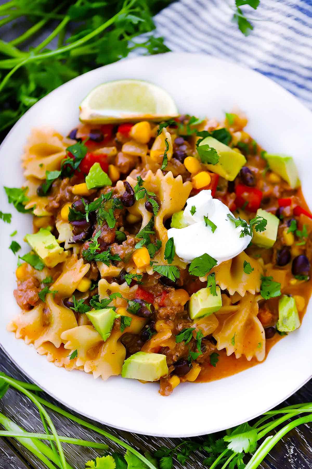 A plate of taco pasta with sour cream and avocado on top.