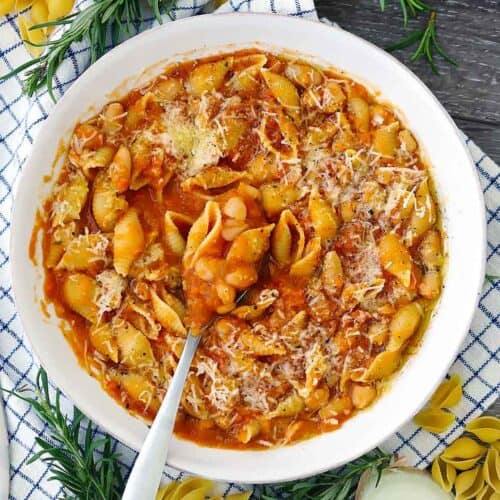 Square photo of an overhead view of a bowl of authentic Pasta e Fagioli in a white bowl with a spoon, topped with grated parmesan cheese.