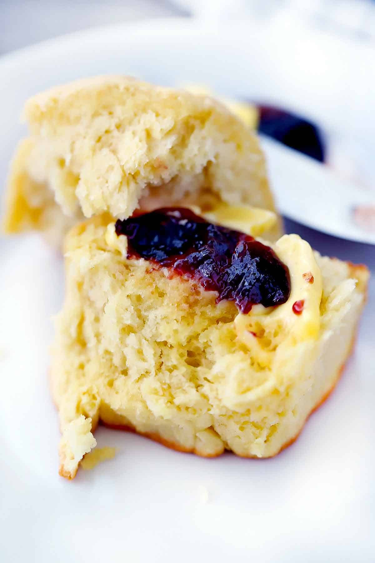 A dinner roll torn in half with butter and jam on it.