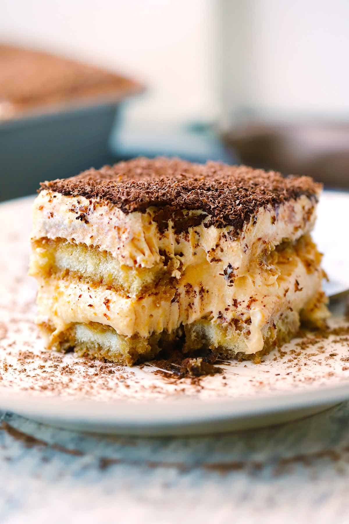 A piece of pumpkin chai tiramisu on a white plate with a bite taken out by a fork.