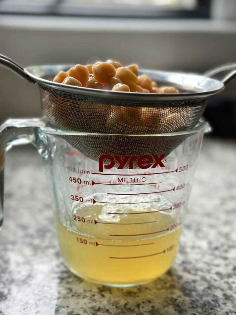 Draining chickpeas in a mesh sieve over a pyrex measuring cup to reserve the liquid.