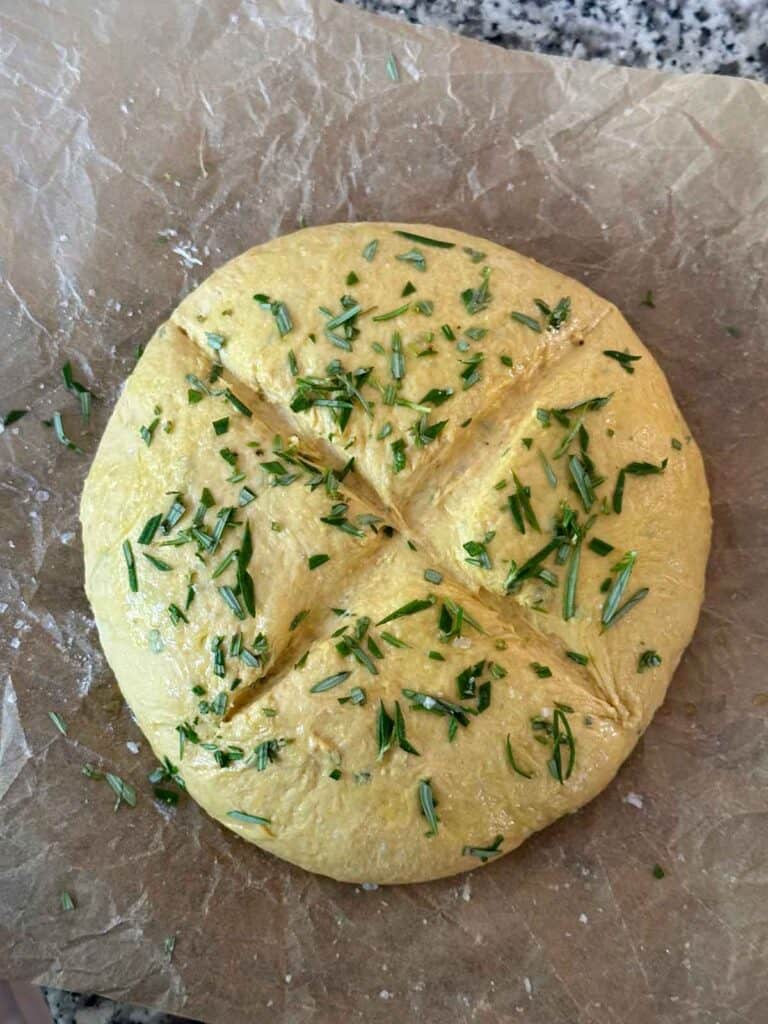A loaf of pumpkin no knead bread with rosemary on top before baking.