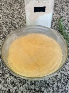 A bowl with pumpkin bread dough in it after rising from the yeast, with plastic wrap covering it.