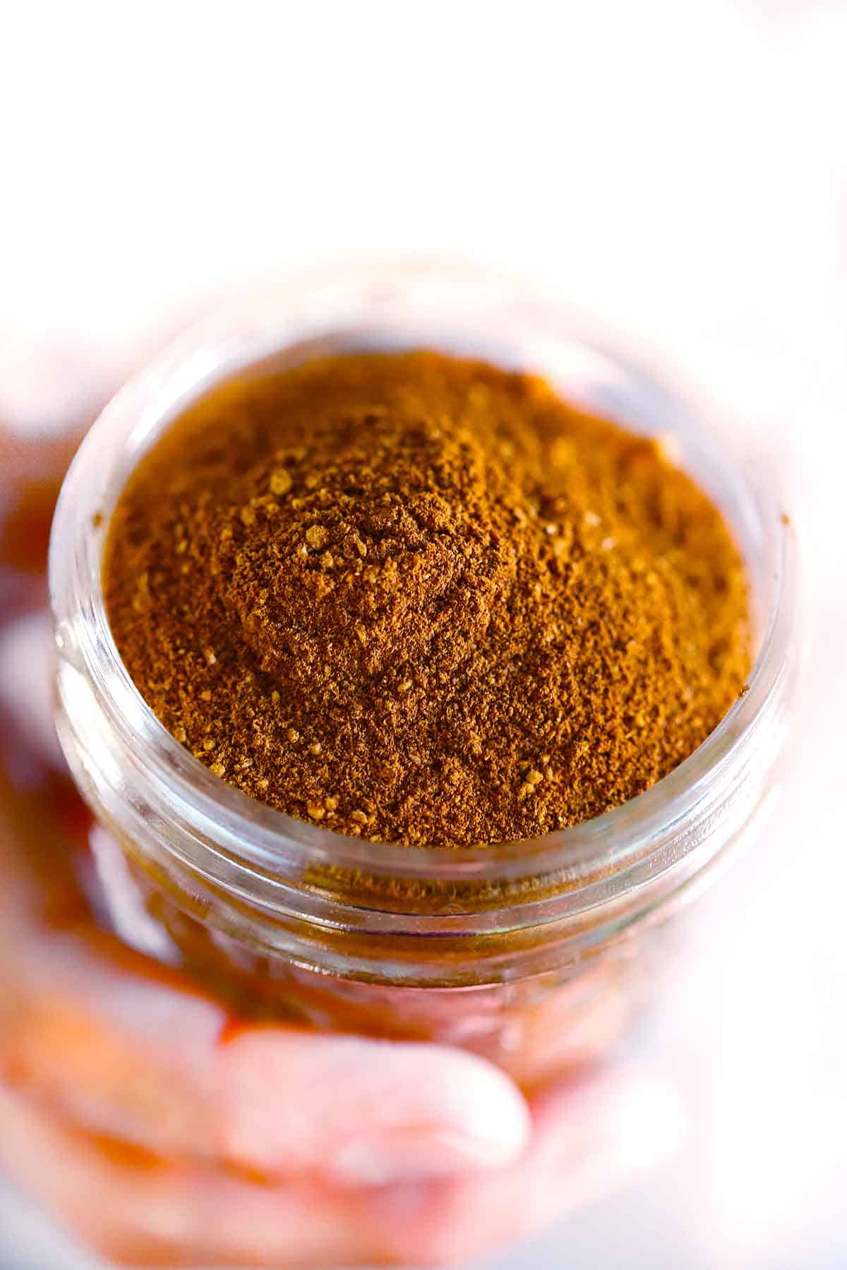 A hand holding a small mason jar of homemade pumpkin pie spice mix.