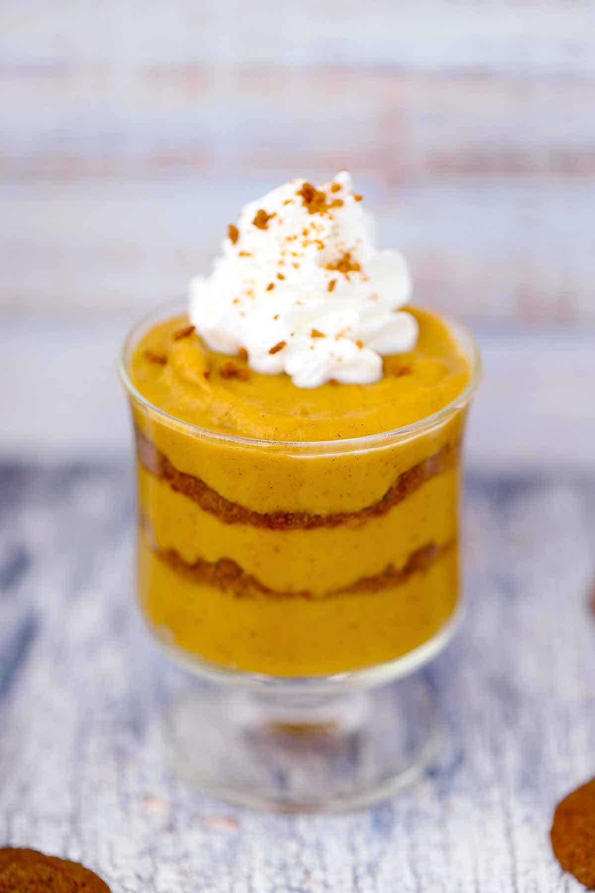 Homemade pumpkin pudding layered in a dessert glass with gingersnap cookie crumbles and whipped cream.