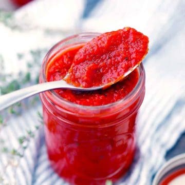 Homemade pizza sauce in a mason jar with a spoon resting on top.