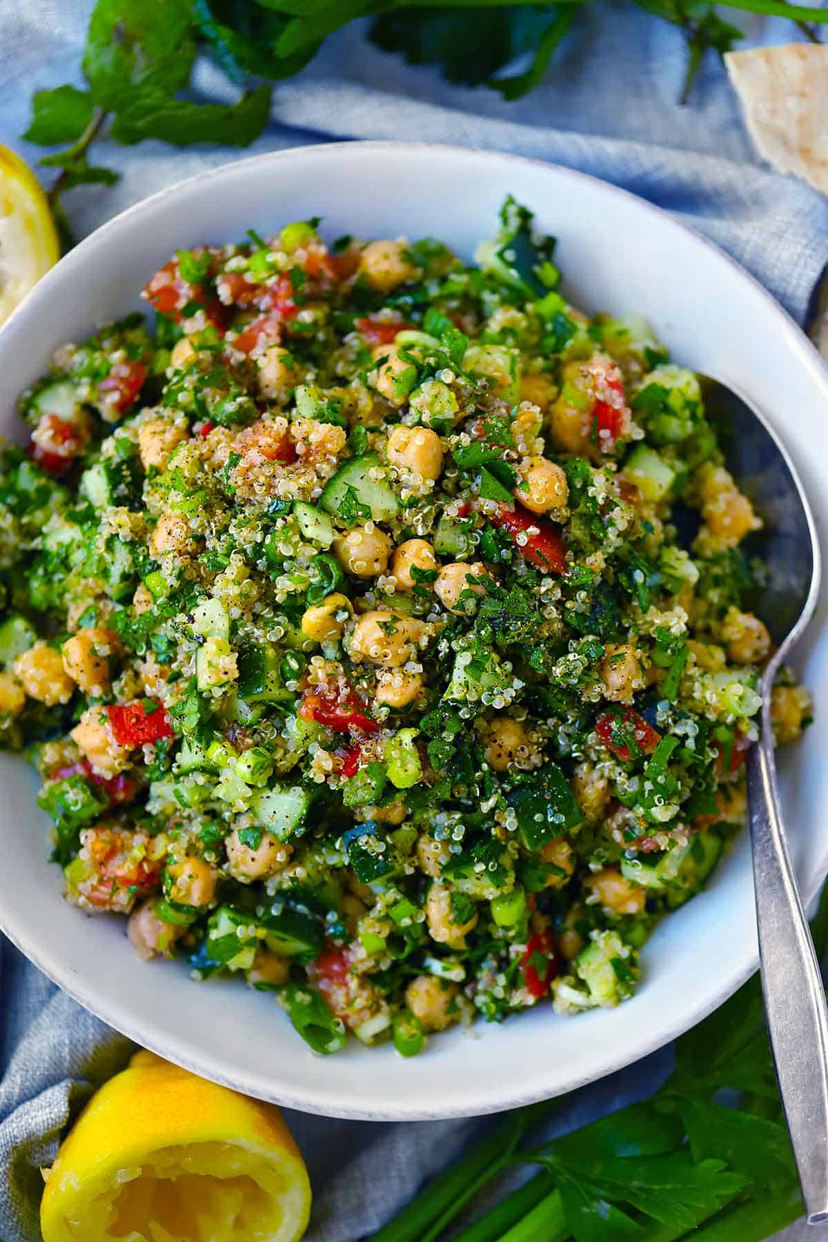 A serving bowl with quinoa chickpea tabbouleh salad in it and ingredients scattered around.