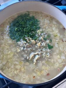 Adding fresh herbs and canned clams to chowder in a Dutch oven.