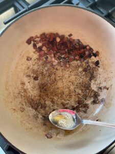 Scooping excess bacon grease from a pot using a spoon.