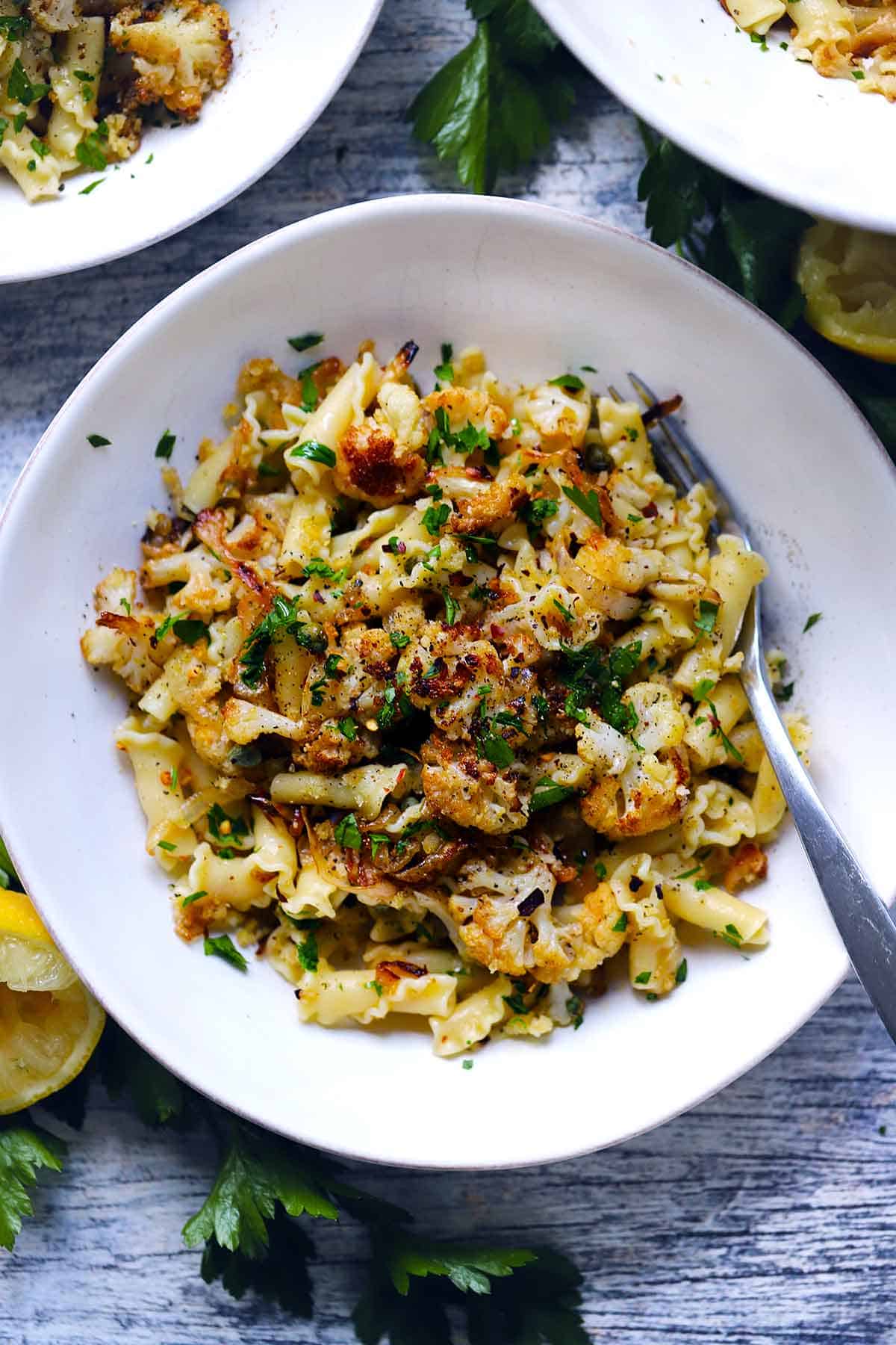 Overhead view of a bowl of roasted cauliflower pasta with a fork in it, garnished with parsley and crispy breadcrumbs.