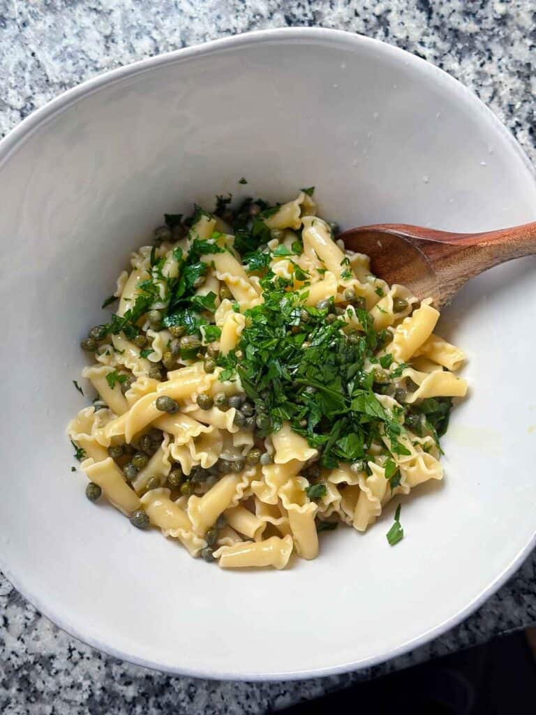 Mixing warm pasta, capers, parsley, and olive oil in a bowl.