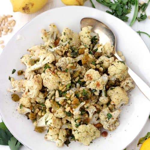 This roasted cauliflower with pine nuts and raisins is a delicious side dish served warm or cold. Tossed with a lemon and olive oil vinaigrette and fresh parsley, it's a fresh Mediterranean recipe that goes with just about anything! Capers or olives can be substituted for raisins for a saltier, lower carb version.