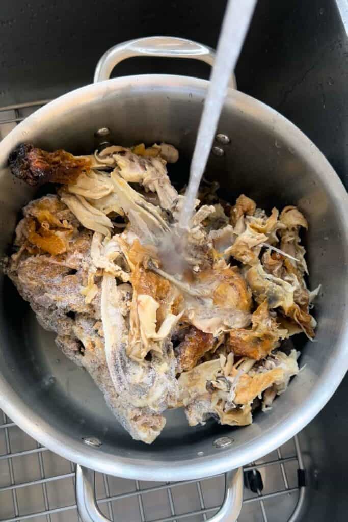 Adding water to a pot with three rotisserie chicken carcasses in it to make homemade bone broth.