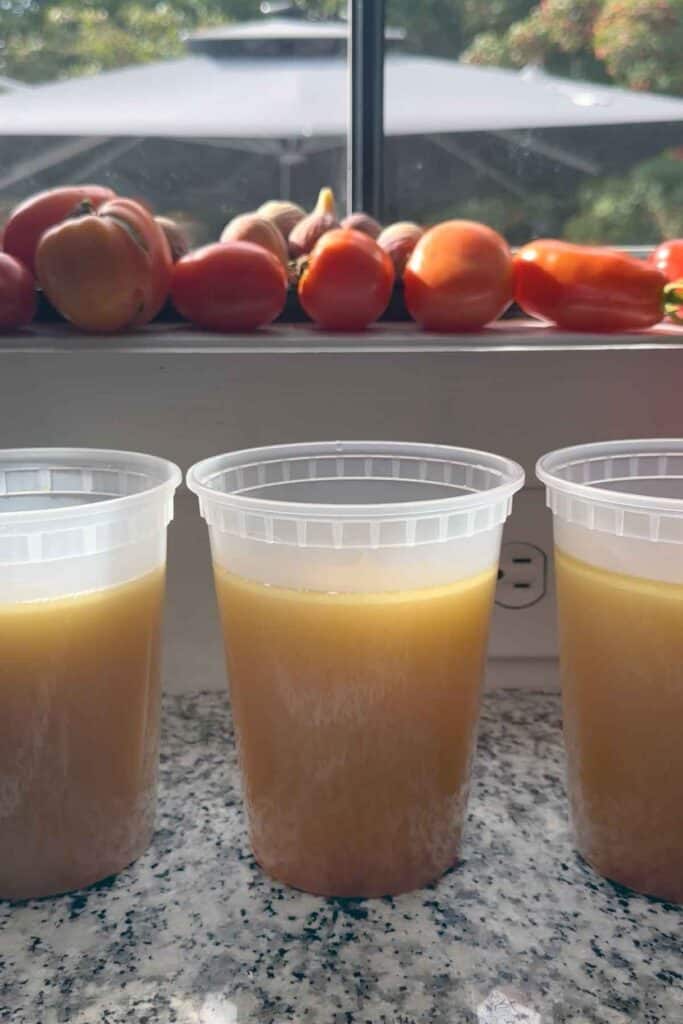Homemade chicken bone broth cooling in containers on the counter before going into the refrigerator.