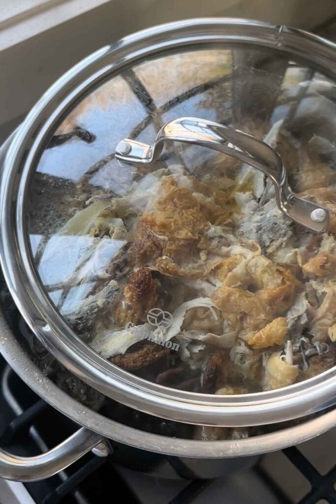 A pot with the lid on ajar to show how to simmer homemade chicken bone broth on low so some of the liquid reduces.