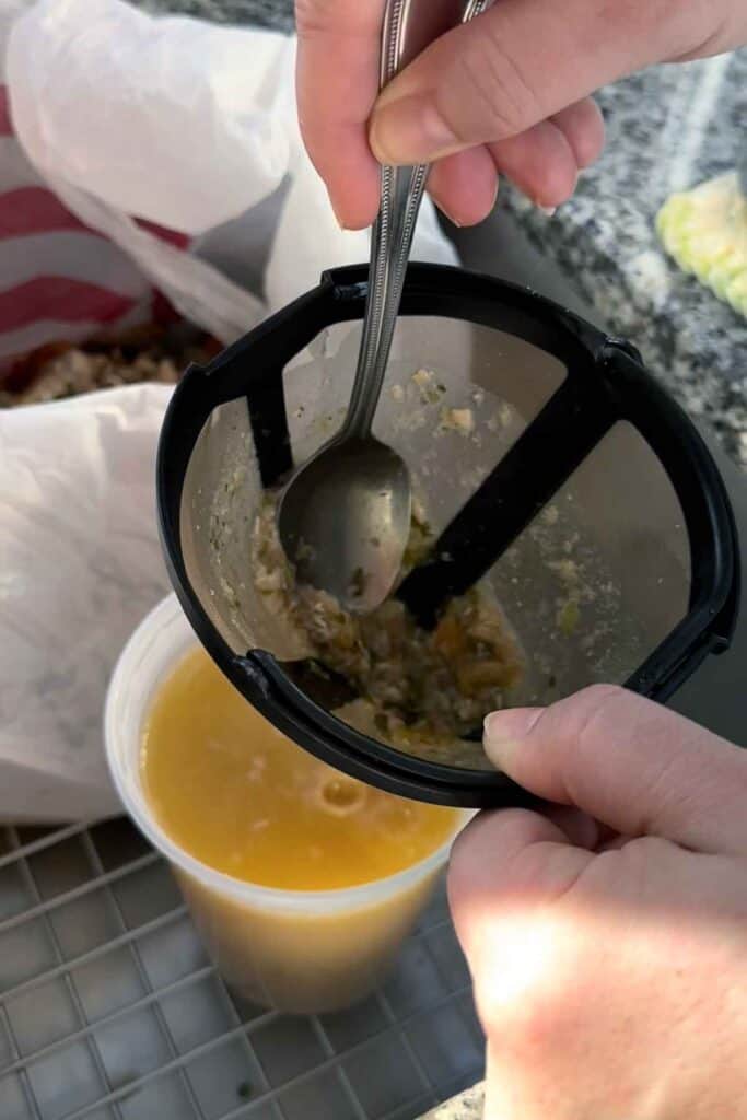 Using a spoon to squeeze out the liquid from remains of chicken broth left in a coffee filter.