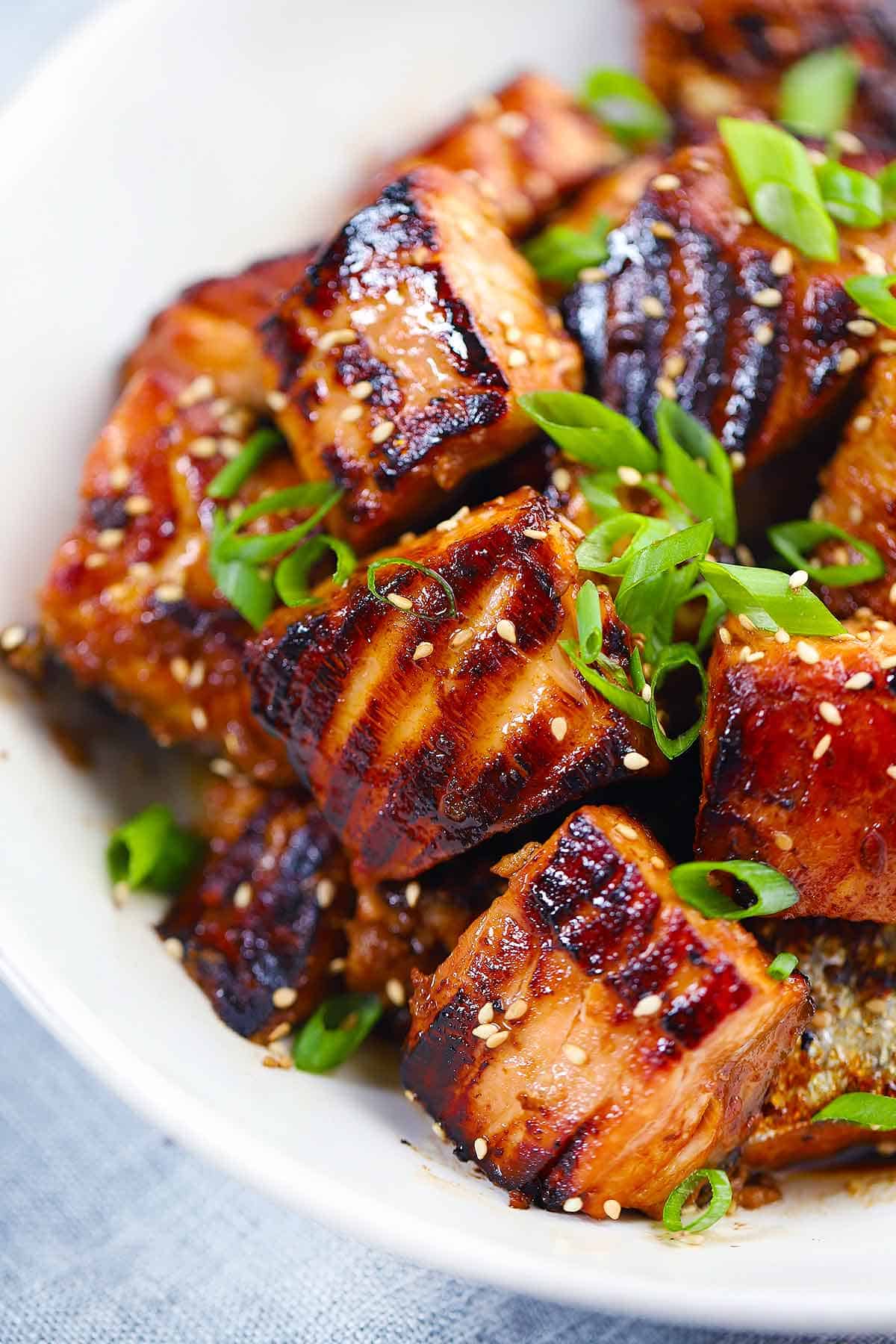 Close up photo of salmon bites in a white bowl with green onions and sesame seeds on top.