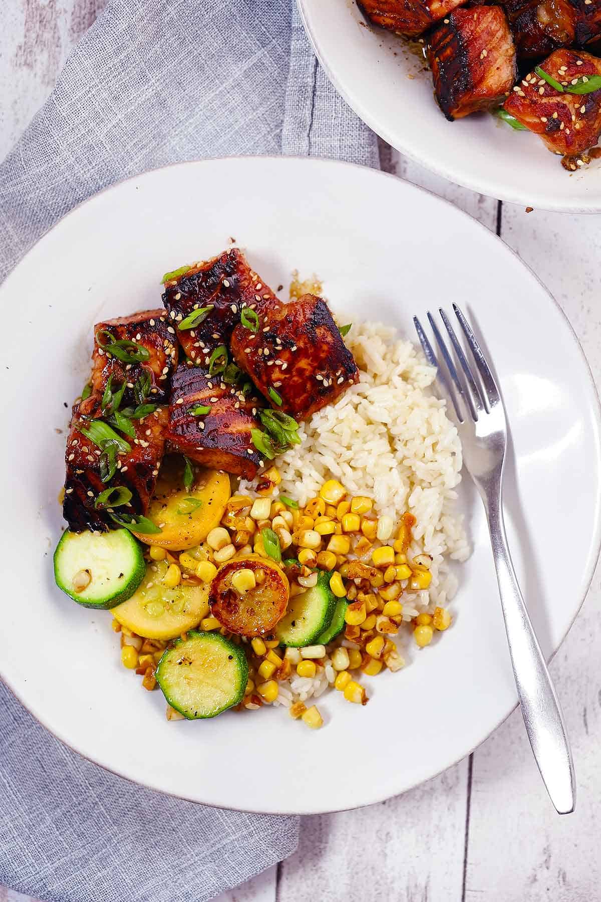 Salmon bites, sautéed corn and zucchini, and rice on a white plate with a fork.