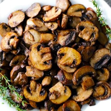 A white plate with sautéed mushrooms and sprigs of thyme.