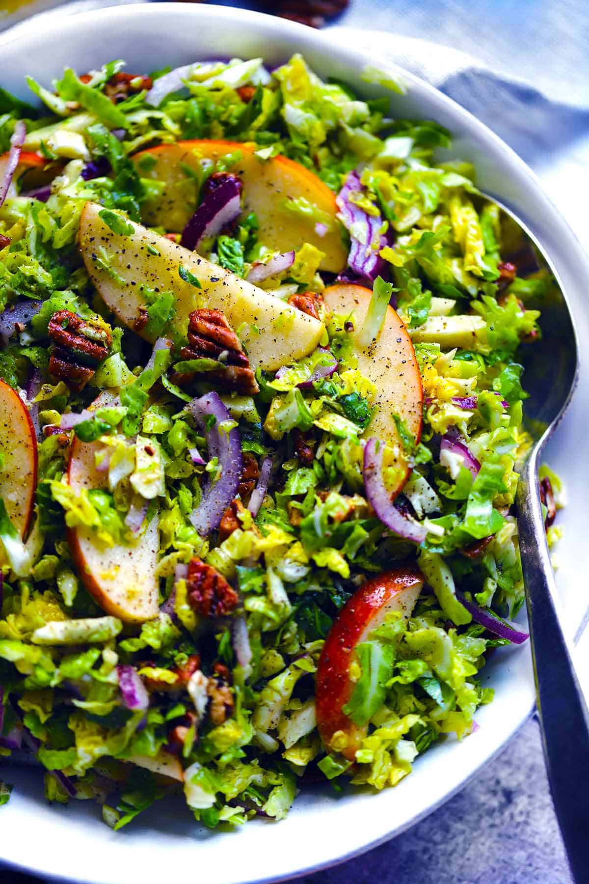 Overhead photo of a shaved Brussels sprouts salad with apples and pecans in a white bowl, close up.