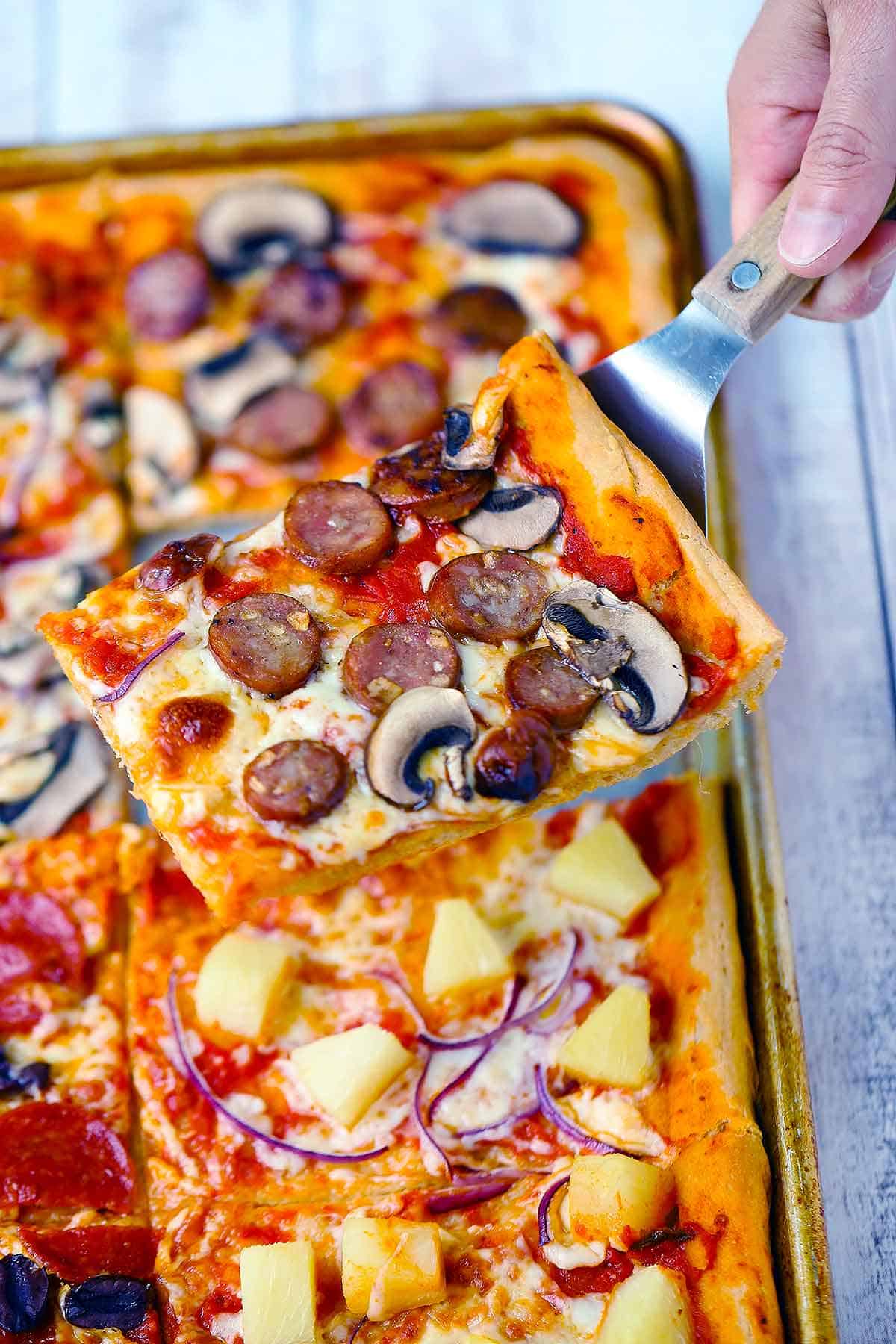 A slice of sheet pan pizza being served on a spatula.