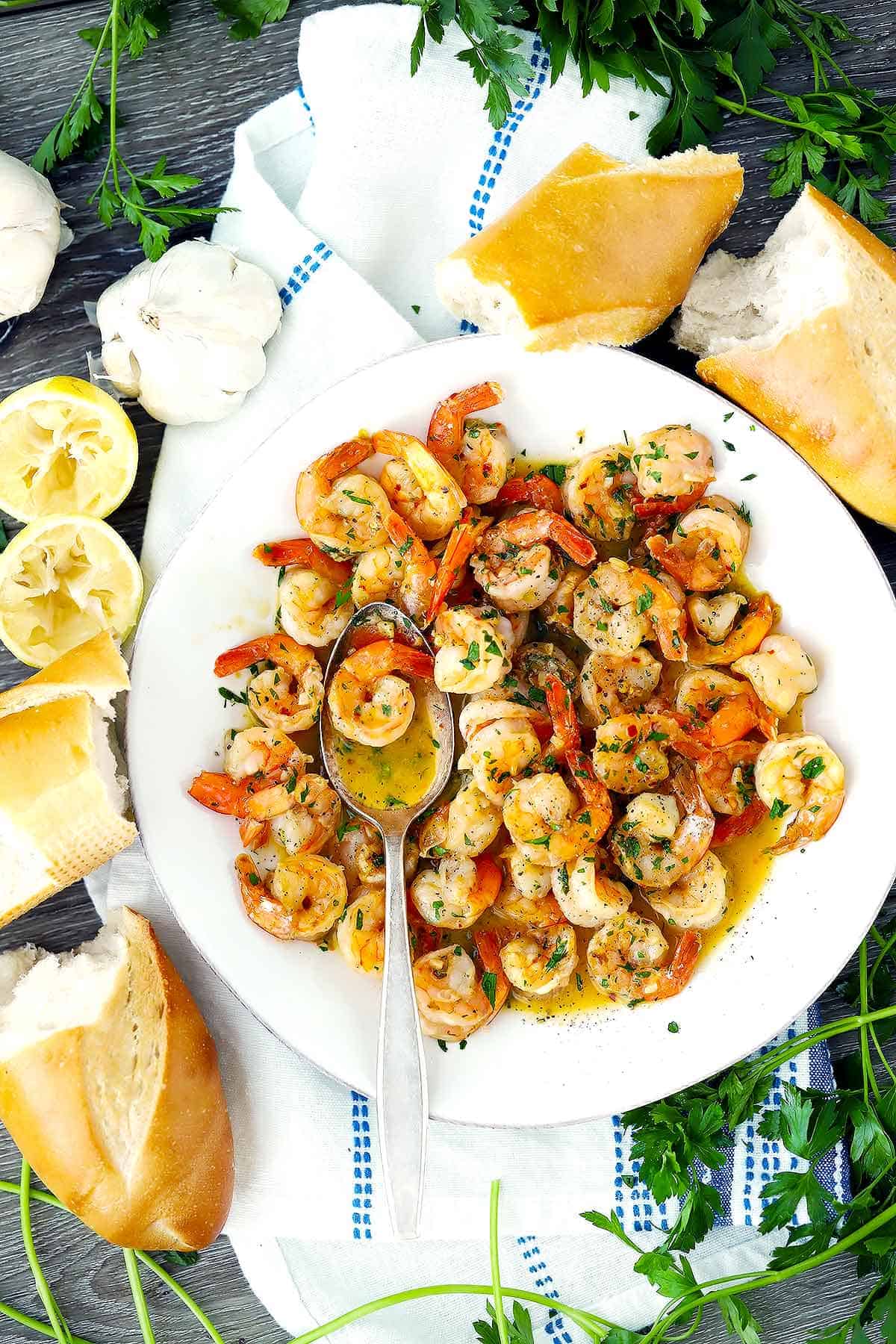 Overhead photo of shrimp scampi with crusty bread on a white plate.