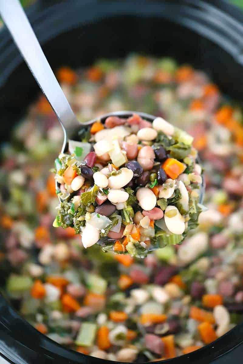 Close up photo of a ladle full of 15 bean soup with ham and kale.