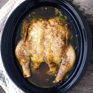 A slow cooker with a whole chicken and chicken stock in it.