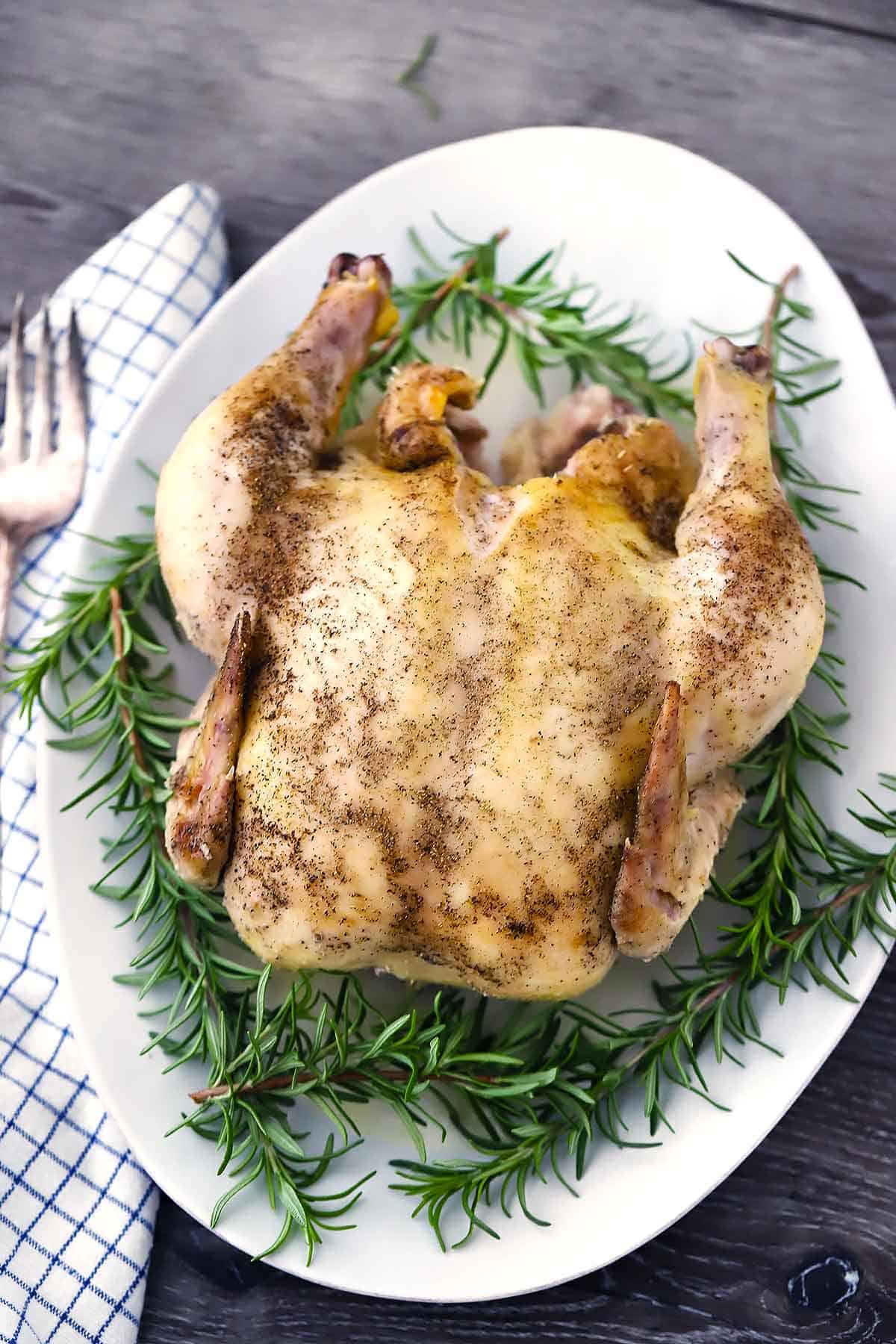 A platter with a whole chicken and rosemary sprigs.