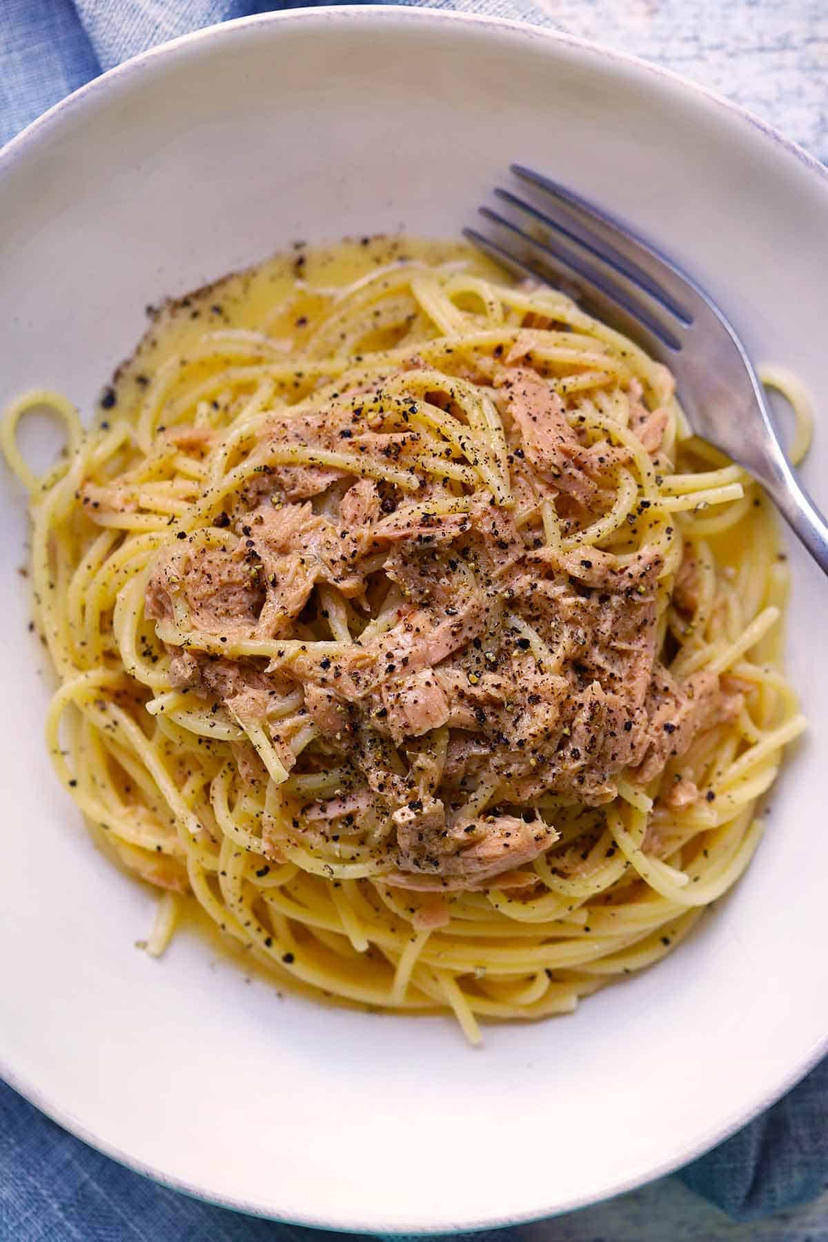 Overhead photo of Spaghetti Tonno e Burro, spaghetti with tuna and butter, with a fork and topped with black pepper.
