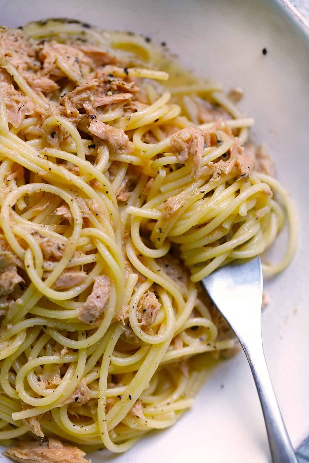 A fork twirling a bite of spaghetti with tuna and butter.