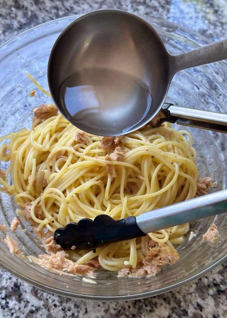 Ladling pasta water into a bowl of spaghetti with tuna and butter.