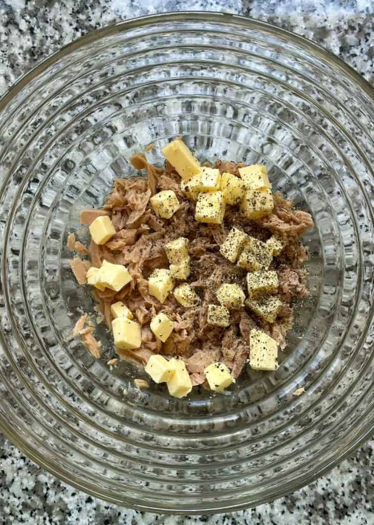 Tuna packed in oil, flaked apart in a large bowl, topped with cubed butter and fresh cracked black pepper.