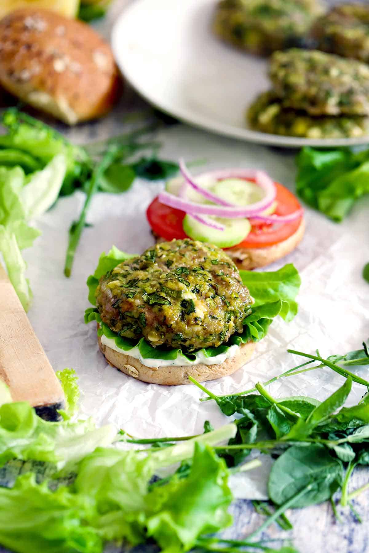 A spanakopita turkey burger open on a bun with ingredients scattered around it.