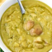 A white bowl with vegetarian split pea soup and a spoon scooping out potatoes from it.