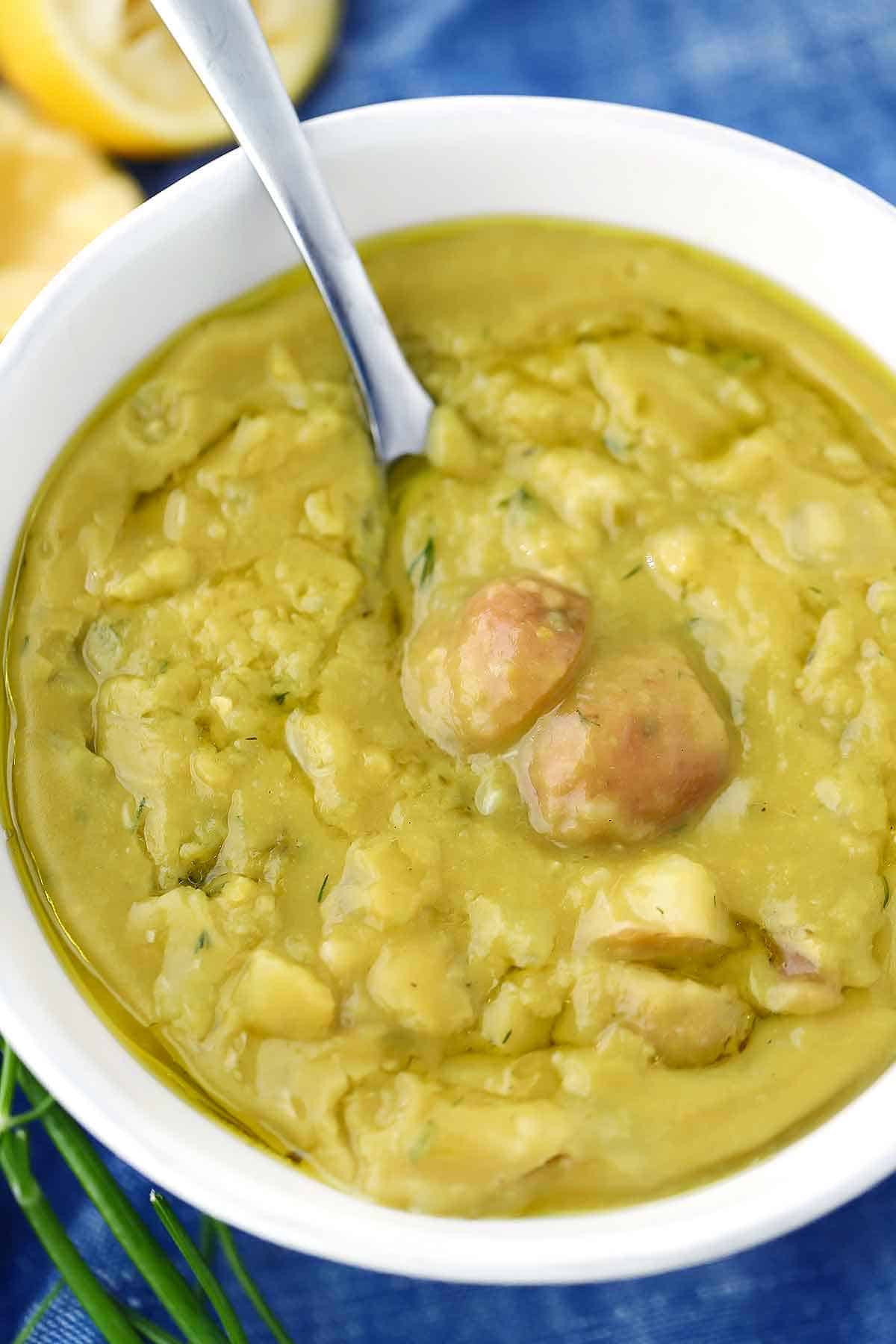 A white bowl with vegetarian split pea soup and a spoon scooping out potatoes from it.