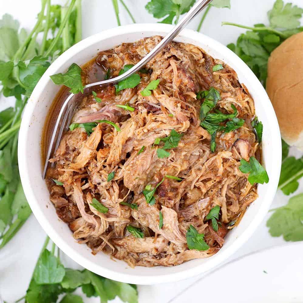 A bowl of pulled pork with a spoon garnished with cilantro