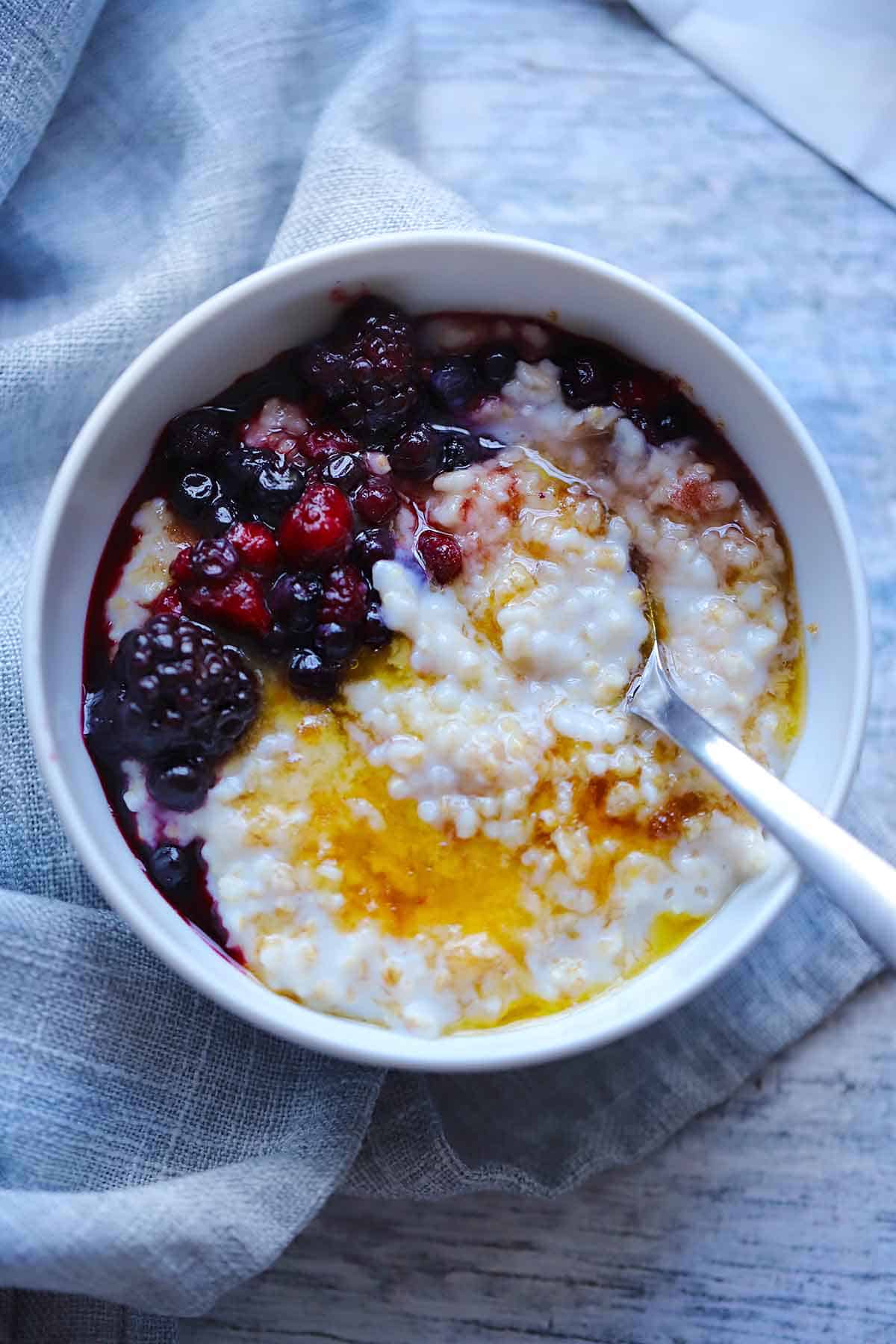 An overhead photo of a bowl of steel cut oatmeal with berries, brown sugar, and butter on top and a spoon in the bowl.