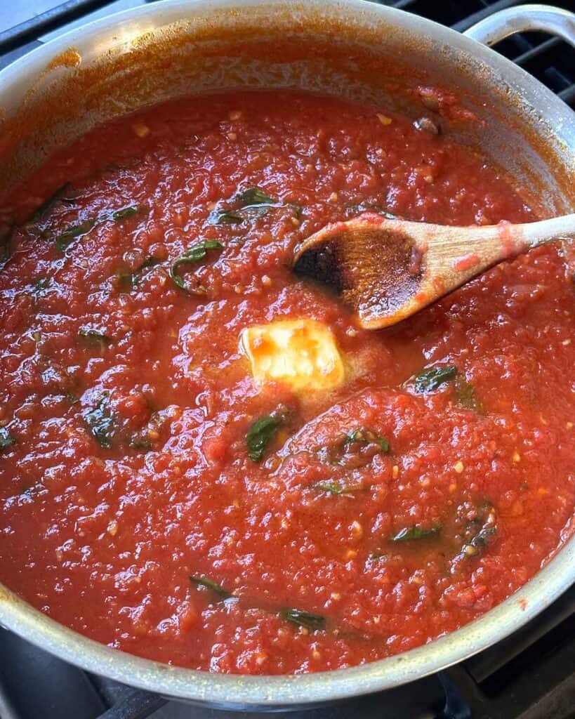 Stirring in a pat of butter into a red tomato sauce.