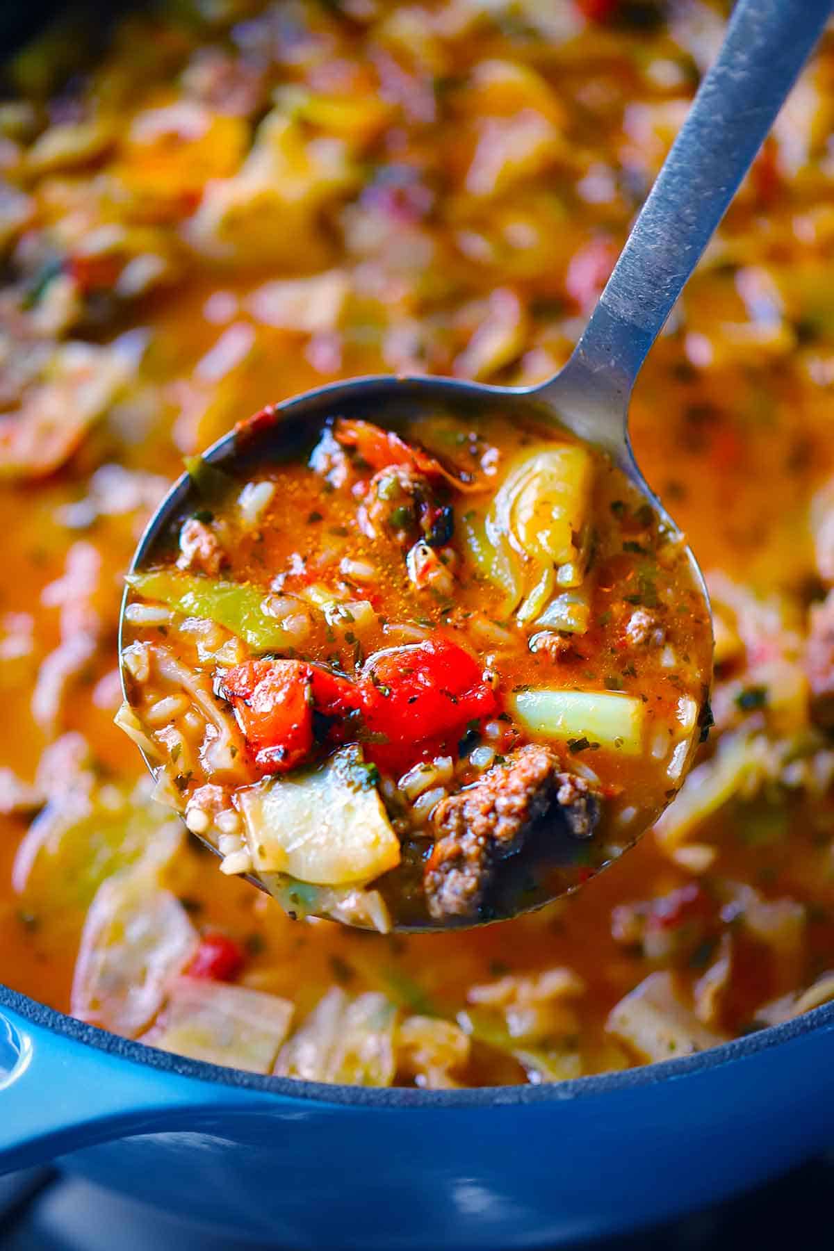 A ladle lifting out a scoop of stuffed cabbage roll soup from a Dutch oven.