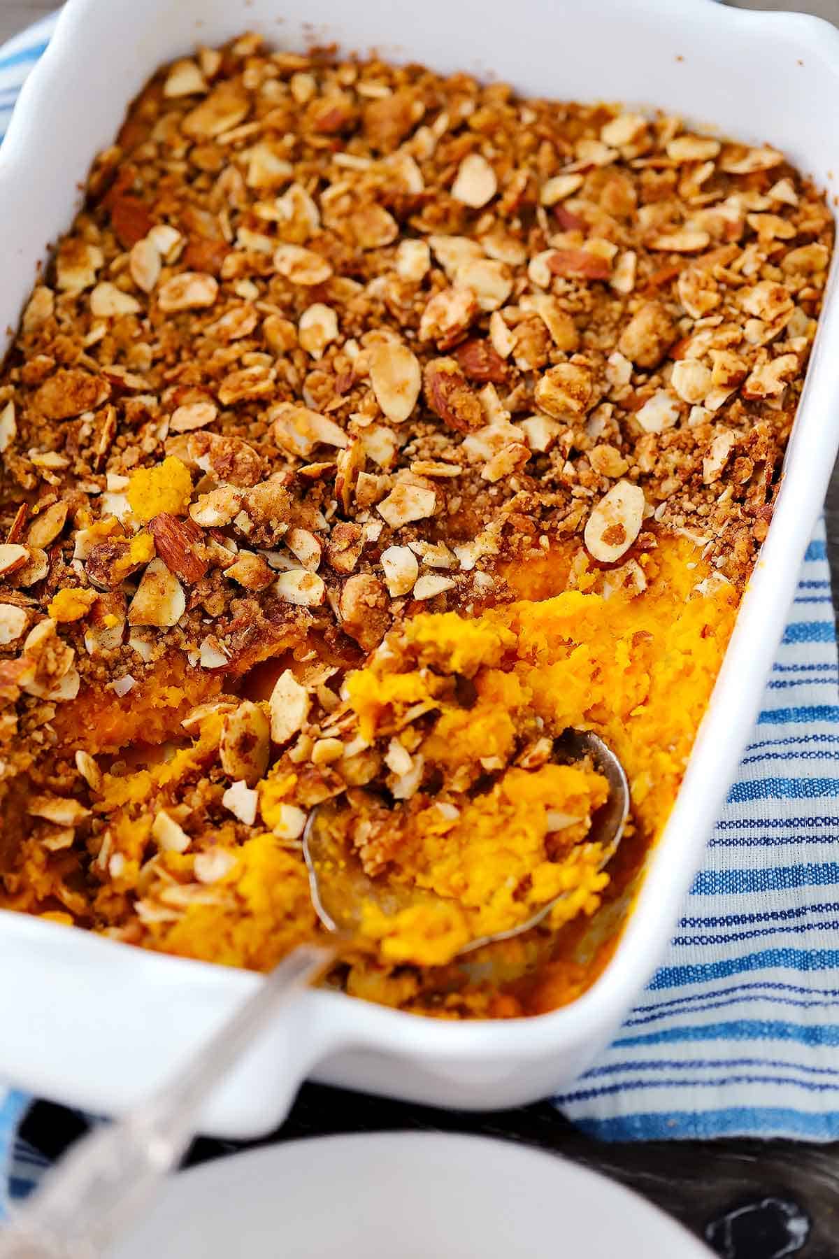 A casserole dish with sweet potato casserole and a spoon taking a scoop out.