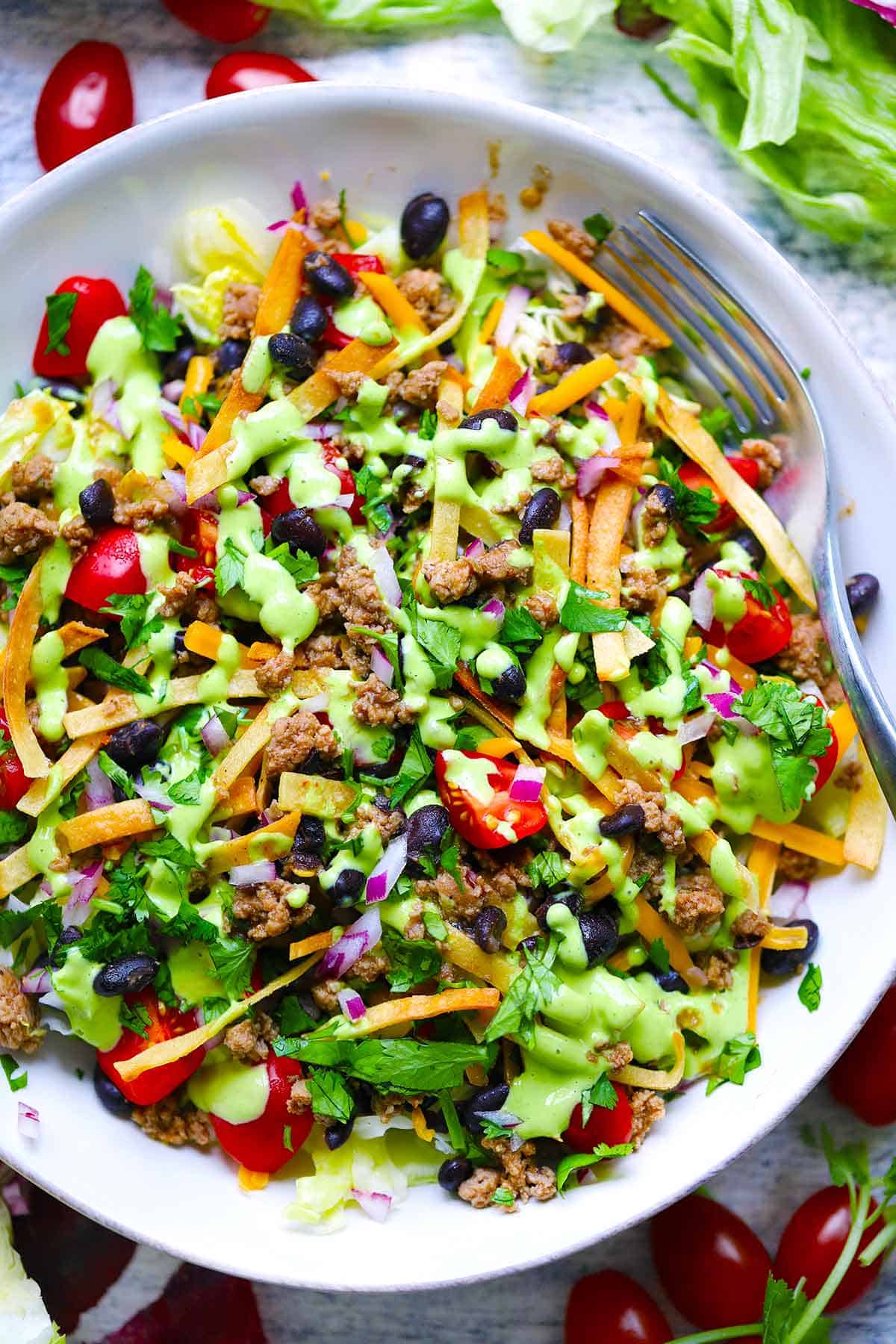 Overhead photo of a bowl of taco salad with avocado cilantro dressing, ground turkey, black beans, and tortilla strips.