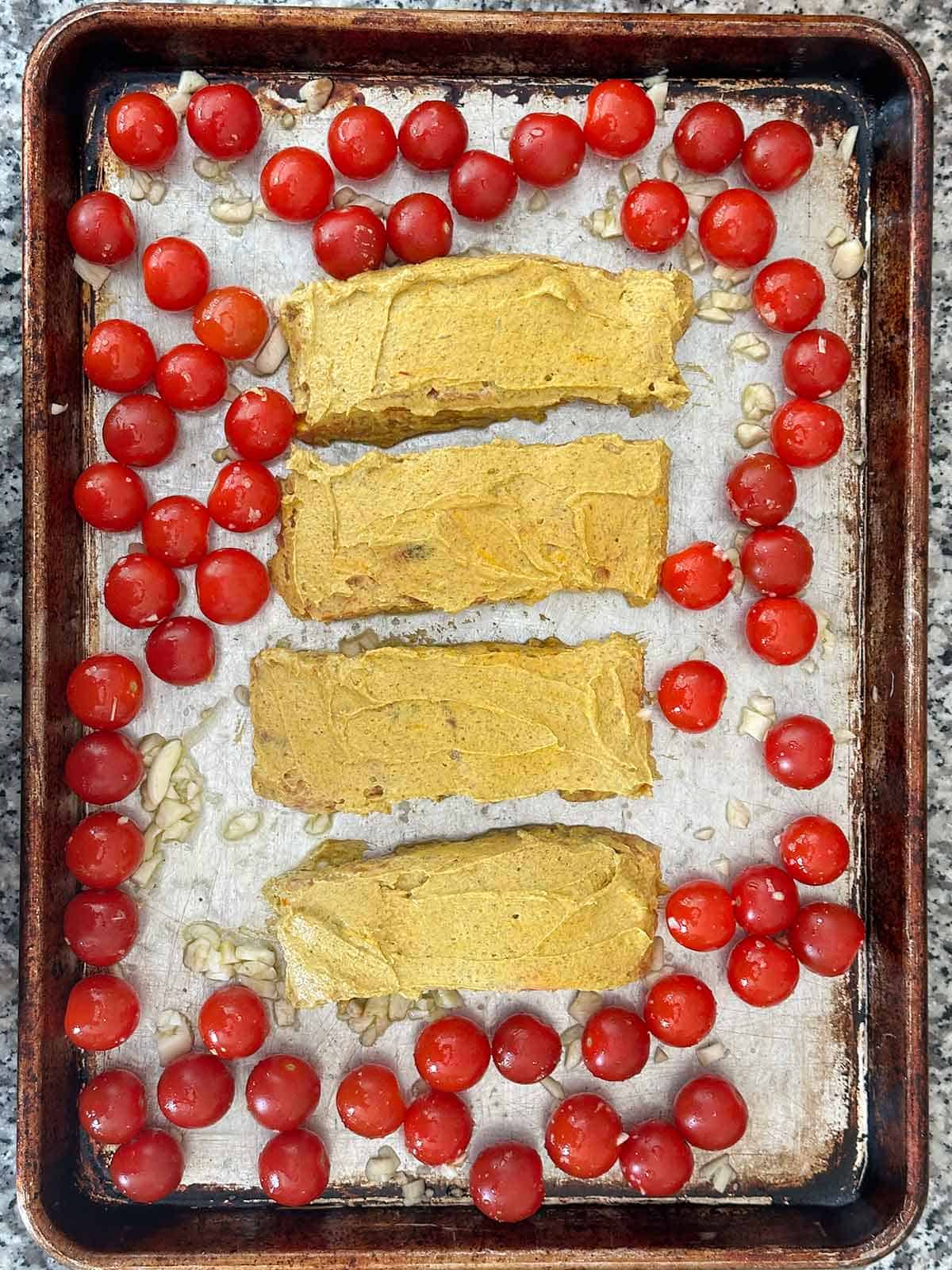 A sheet pan with cherry tomatoes and yogurt marinated tandoori salmon before cooking.