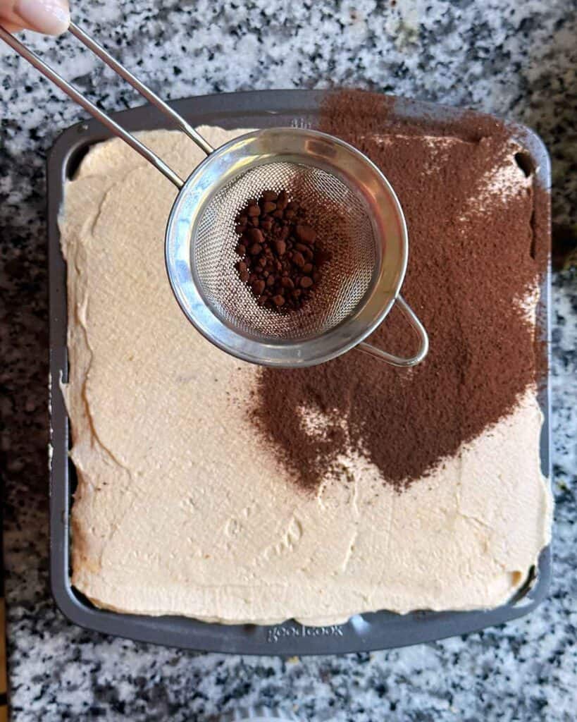 Dusting the top of a pumpkin chai tiramisu with cocoa powder and pumpkin pie spice mix.