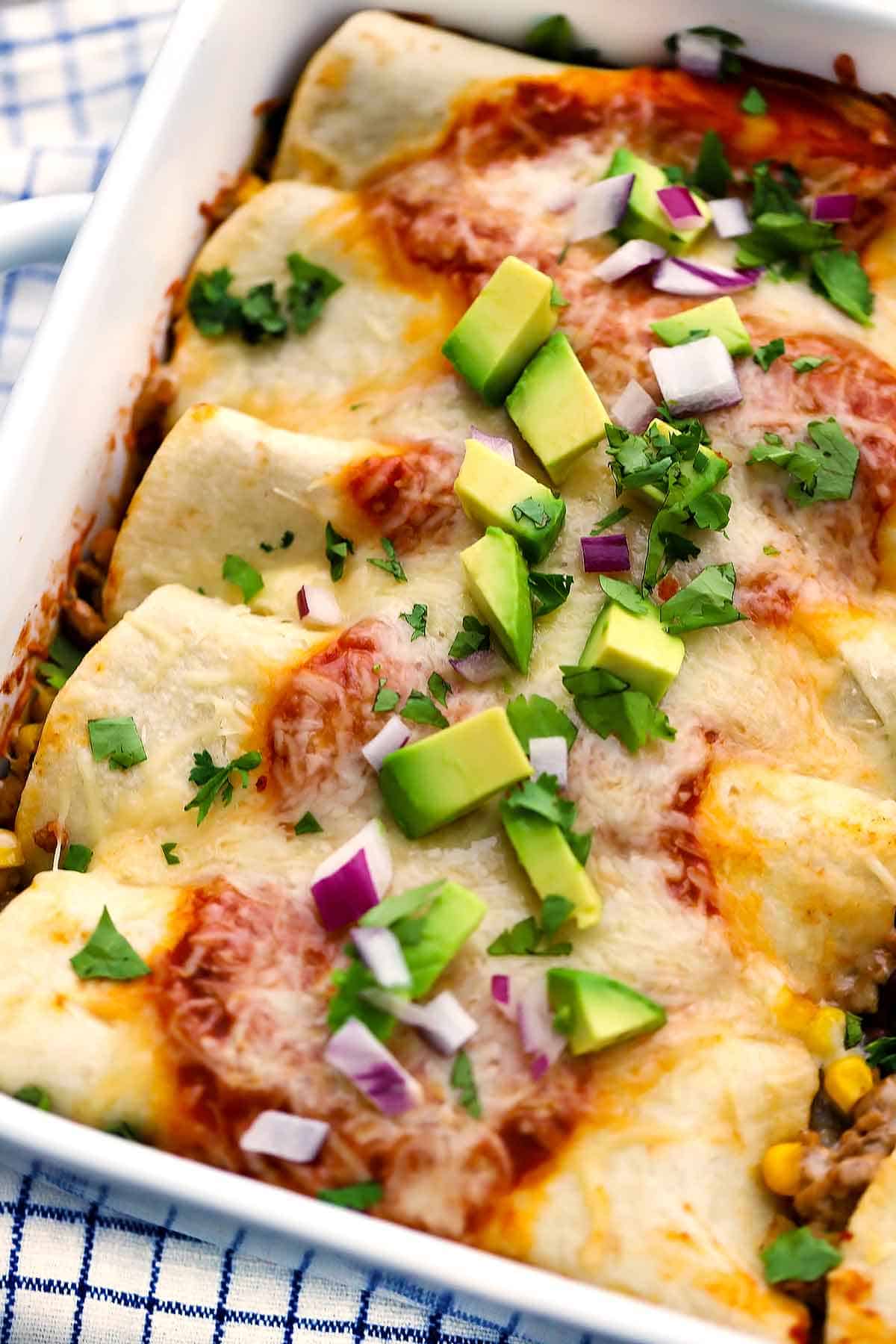 Close up photo of turkey and black bean enchiladas with diced avocado and red onion on top.