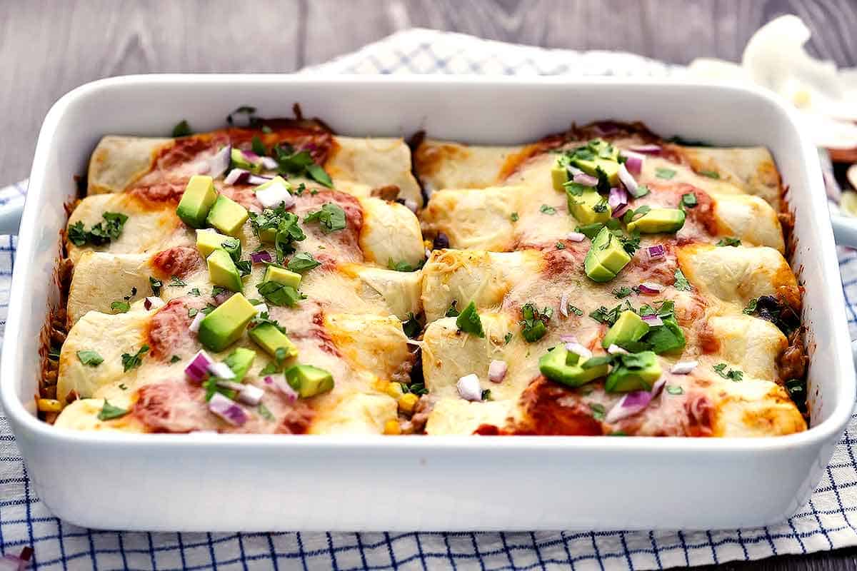 Horizontal photo of a white 9 by 13 baking dish with enchiladas inside.
