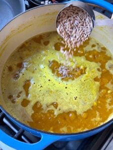Adding orzo to turmeric soup.